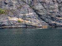 Mit weißen Schichten durchzogene Felswand über der Uferlinie - Aurlandsfjord